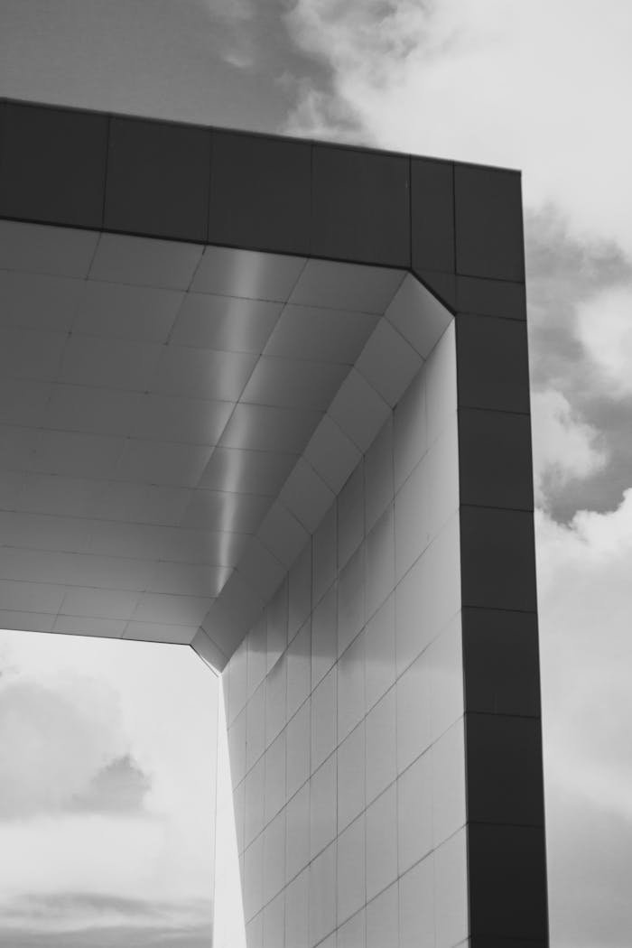 our-journey-03 Monochrome shot capturing the geometric elegance of a modern architectural archway against a cloudy sky.